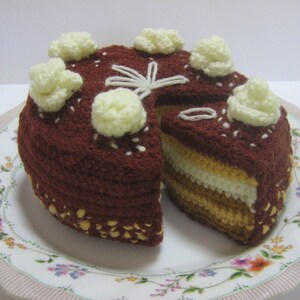 Può includere: Una torta all'uncinetto con glassa marrone e glassa bianca. La torta è decorata con rosette di glassa bianca e si trova su un piatto bianco con un motivo floreale.