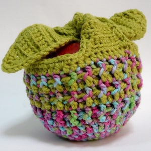 Op de afbeelding: Een groene gehaakte appelwarmer met een roze, groene en blauwe gepatroneerde bodem.