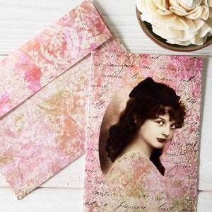May include: A vintage-style card with a pink and white floral pattern. The card features a black and white photo of a woman with dark hair and a white dress. The text on the card reads "Le Gallard, en est arriv&eacute; me dire que la fleur", which is French for "The Gallard, has arrived to tell me that the flower".
