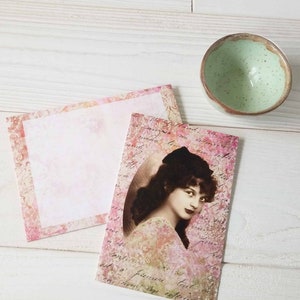 May include: A vintage-style card with a pink and white floral design. The card features a black and white photo of a woman with dark hair and a white dress. The text on the card is in a cursive font and reads "The only thing I need is you".