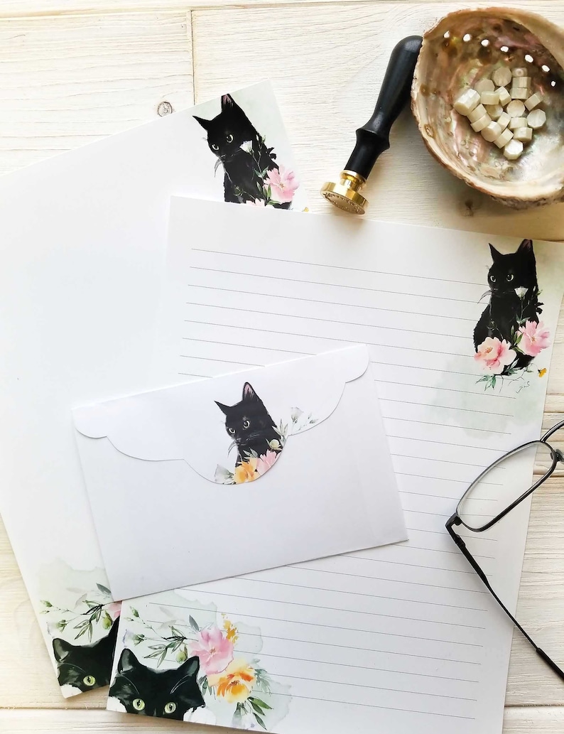May include: A set of stationery featuring black cats with floral accents. The set includes a letter writing sheet, envelope, and a smaller card with a scalloped edge. The stationery is perfect for sending handwritten notes.