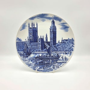 May include: Blue and white ceramic plate featuring a depiction of the Houses of Parliament and Big Ben in London, England. The plate has a blue and white design with a border of small blue flowers. The text "Big Ben" is printed on the bottom of the plate.