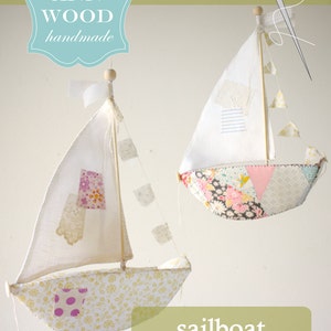 May include: A sewing pattern for a sailboat, featuring two fabric sailboats with patchwork designs. The sailboats are suspended from the ceiling. The pattern is titled "sailboat, a sewing pattern".