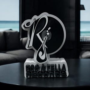 Könnte beinhalten: Eine weiße und schwarze 3D-gedruckte Skulptur des Roc-A-Fella Records-Logos. Das Logo zeigt einen stilisierten Buchstaben "R" mit einer Schallplatte darin. Die Basis der Skulptur trägt die Aufschrift "Roc-A-Fella Records".