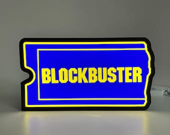 May include: A black and yellow neon sign shaped like a movie ticket with the word "BLOCKBUSTER" in yellow letters on a blue background.