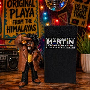 May include: A figurine of a man in a brown jacket and black pants saluting, next to a black box with the name "MARTIN" on it. The background includes a disco ball, string lights, and signs that read "ORIGINAL PLAYA FROM THE HIMALAYAS" and "DO THE RIGHT THING".