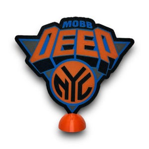 May include: Orange and blue 3D printed logo with the text "MOBB DEEP" and "NYC" in a triangle shape. The logo is on a small orange stand.
