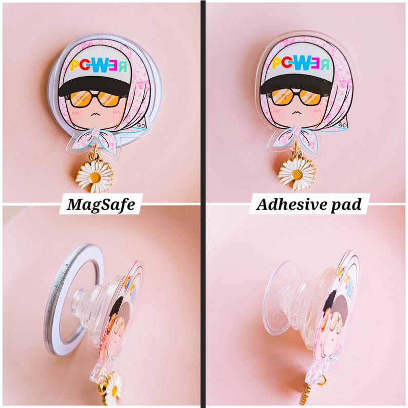 May include: A clear phone grip with a cartoon illustration of a person wearing sunglasses and a headscarf, with the word "POWER" in colorful letters. The grip has a daisy charm and is available in MagSafe and adhesive pad options.