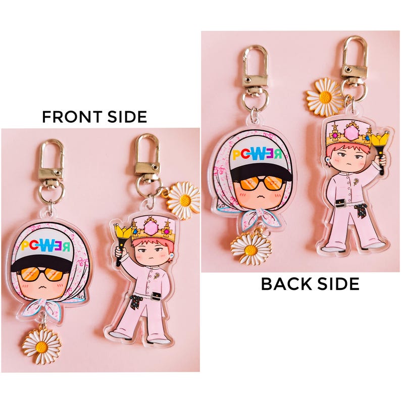 May include: Two clear acrylic keychains with cartoon illustrations. One keychain features a character wearing a headscarf and sunglasses, the other a character in a pink uniform holding a torch. Both have daisy charms and silver-tone hardware.