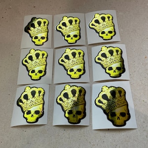 May include: Nine yellow and black holographic stickers with a skull wearing a crown. The crown has the word "Boss" written on it.