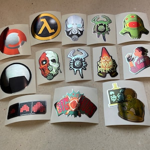 May include: A selection of stickers with various designs. The stickers feature images of video game characters, logos, and text. The stickers are on a neutral background.