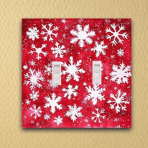 May include: A red light switch cover with a white snowflake pattern. The switch cover has two toggle switches.