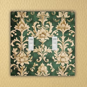 May include: A double light switch cover with a green and gold damask pattern. The switch cover has two white toggle switches.
