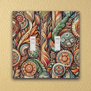 May include: A double light switch cover with a colorful, abstract design featuring swirls, leaves, and flowers in shades of orange, brown, green, blue, and yellow.