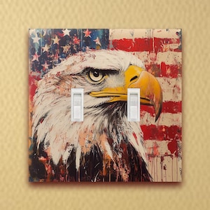 May include: A light switch cover featuring a close-up of a bald eagle with a distressed American flag background. The eagle's head is turned to the right, and its eye is visible. The switch cover has two white toggle switches.