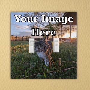 May include: A decorative light switch cover featuring a photograph of a cat in a grassy field with the text "Your Image Here". The cover has two light switch openings and is set against a yellow wall.