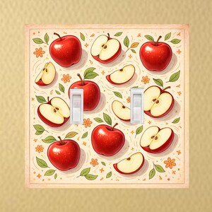 May include: A square double light switch cover plate featuring a cream-colored background with a repeating pattern of whole red apples, sliced apple segments, small green leaves, and tiny orange flowers across the entire surface area.