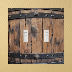 May include: A decorative light switch cover featuring a rustic design. The cover is made to look like a wooden barrel, with dark metal bands and two white light switches. The wood has a natural, aged appearance.