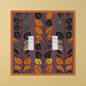May include: A decorative light switch cover featuring a repeating pattern of stylized leaves in shades of green, orange, and black against a purple background. The cover has a brown border and two white light switches.