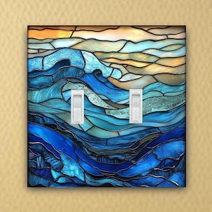 May include: A decorative light switch cover featuring a stained-glass design of ocean waves in shades of blue, teal, and gold. The cover has two white light switches. The background is a textured, light yellow wall.