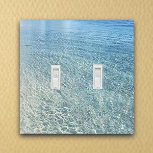 May include: A light blue and white double light switch cover with a photo of clear blue water with ripples and waves.