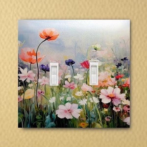 May include: A double light switch cover plate featuring a colorful floral meadow print. The design displays various painted flowers in shades of pink, orange, purple, and white against a soft, light-colored background with two white toggle switches.