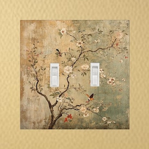 May include: A light switch cover with a vintage floral design featuring a blooming tree with birds and butterflies. The background is a faded blue and green with a textured look.