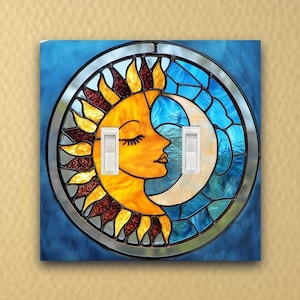 May include: A stained glass light switch cover featuring a sun and moon design. The sun is yellow with a human face and the moon is blue and crescent shaped.