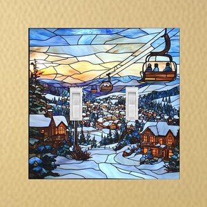 May include: A stained glass style light switch cover featuring a winter scene with a ski lift, houses, and a snowy mountain landscape.