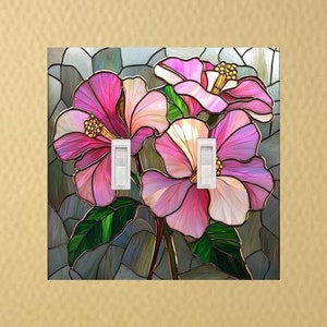 May include: A double light switch cover plate featuring a stained glass style design of three pink hibiscus flowers with green leaves against a gray background. The plate has two white toggle switches centered within the floral artwork.