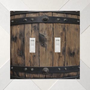 May include: A double light switch wall plate featuring a high-resolution print of a rustic wooden barrel with dark brown vertical planks, black metal bands, and decorative rivets. Two white vertical toggle switches are centered on the plate.