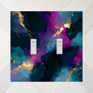 May include: A double light switch wall plate featuring an abstract painted design with blended shades of deep navy blue, vibrant teal, and bright magenta, accented by thin, flowing streaks of metallic gold throughout the surface.