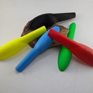 May include: Five colorful plastic spoons, including black, yellow, blue, green, and red, are arranged on a rock-like surface.