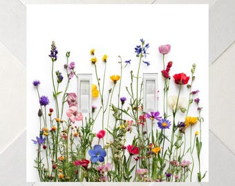 May include: A double light switch wall plate featuring a white background printed with a vibrant array of colourful wildflowers including blue, yellow, pink, red, and purple blossoms, with two rectangular white toggle switches centred.