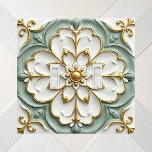 May include: A double light switch wall plate featuring a raised, embossed floral pattern in white, sage green, and metallic gold. The design includes symmetrical scrollwork and a central circular gold accent, with two white toggle switches.