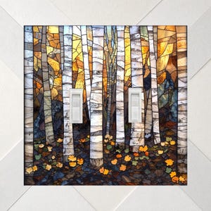 May include: A double light switch cover featuring a stained glass style print of a forest with white birch trees, golden yellow autumn leaves, and a dark ground. The rectangular plate has two white toggle switches centered on the design.