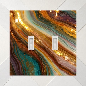 May include: A double light switch wall plate featuring a fluid acrylic pour design with swirling patterns of metallic gold, deep teal, copper, and purple. The rectangular cover includes two white vertical toggle switches centered.
