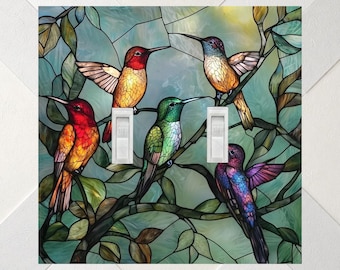 May include: A double light switch cover plate featuring a stained glass style design of four hummingbirds in red, orange, green, and purple perched on branches amidst green leaves against a light blue and white background.