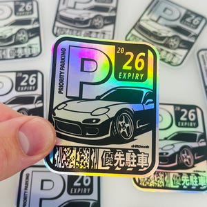 May include: Holographic stickers with a sports car design, the text "PRIORITY PARKING" and "26 EXPIRY". The stickers have a rainbow sheen and Japanese characters. Several stickers are visible.