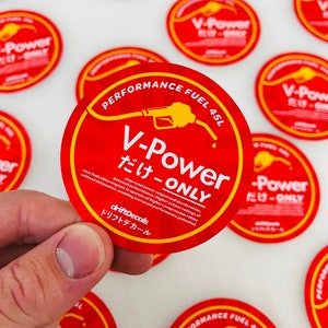 Może przedstawiać: Okrągła naklejka w kolorze czerwonym i żółtym z tekstem "V-Power だけ-ONLY" i grafiką pompy benzynowej. Naklejka zawiera napis "Performance Fuel 45L" i "driftDecals ドリフトデカール".
