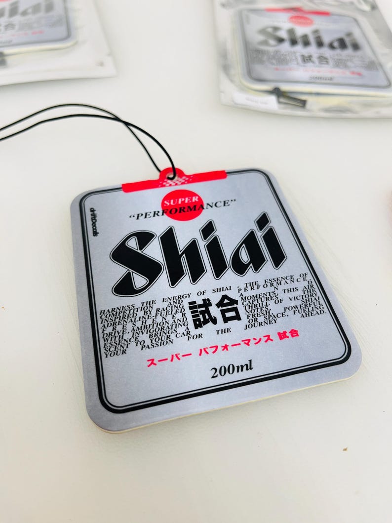 May include: A silver car air freshener with a black and red design. The text "Shiai" is printed in black and red, and the text "Super Performance" is printed in red. The text "試合" is printed in black. The text "スーパー パフォーマンス 試合" is printed in black. The text "200ml" is printed in black.