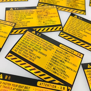 May include: Yellow and black warning stickers with the text "PLEASE FASTEN YOUR SEAT BELT" and "ATTENTION" in English and Japanese. The stickers have a black and yellow striped border.