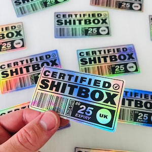 Puede incluir: Un primer plano de una pegatina holográfica que dice "CERTIFIED SHITBOX" con un código de barras y una marca de verificación. La pegatina es de color arcoíris y tiene un fondo negro. La pegatina tiene una fecha de caducidad en 2025 y está marcada con "UK".