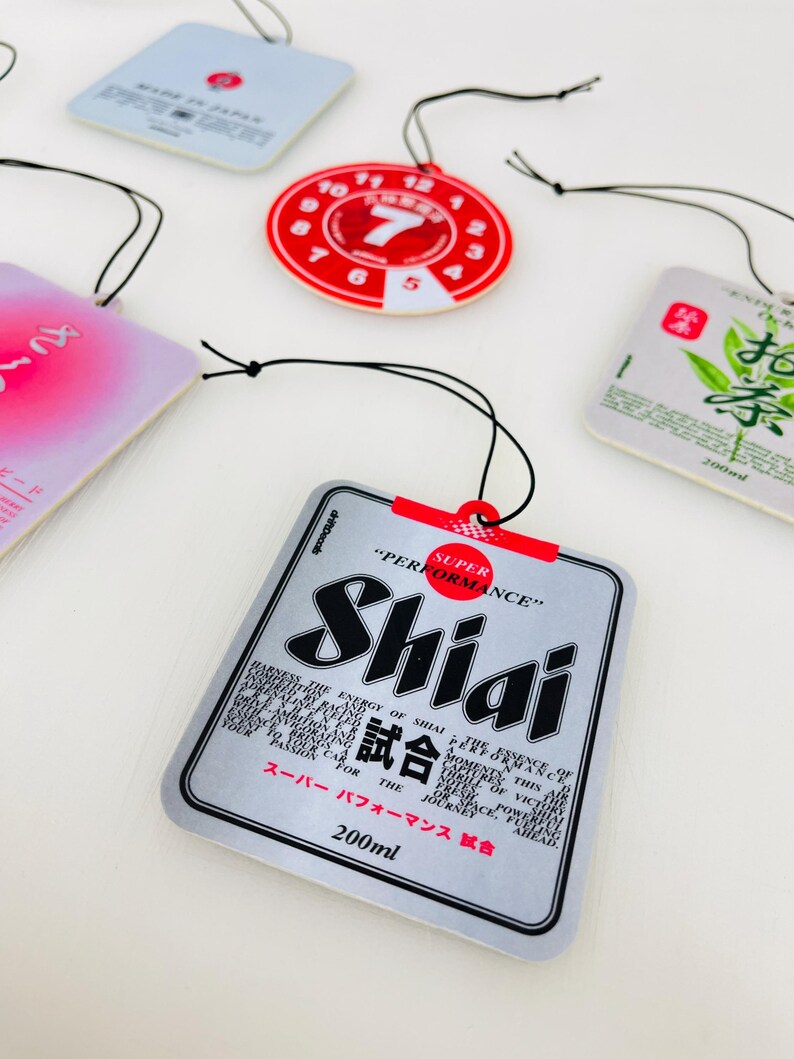 May include: A silver car air freshener with the text "SUPER PERFORMANCE" and "Shiai 試合" in black and red. The text "200ml" is printed in black at the bottom of the air freshener.