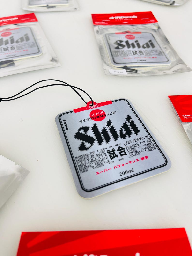 May include: A silver car air freshener with a black string for hanging. The air freshener is shaped like a can and has the text "Shiai 試合" and "Super Performance" printed on it. The air freshener is 200 ml.