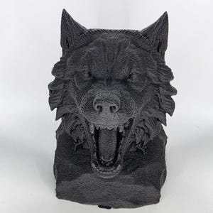 May include: A black, 3D-printed sculpture of a wolf's head, snarling with its mouth open. The sculpture has detailed fur texture and pointed ears. The base is rectangular. The sculpture is approximately 15 cm tall.