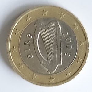 Könnte beinhalten: Eine goldfarbene Münze mit einem silbernen Zentrum, das eine Harfe und den Text "EIRE" und "2002" zeigt. Die Münze hat 12 Sterne am Rand.