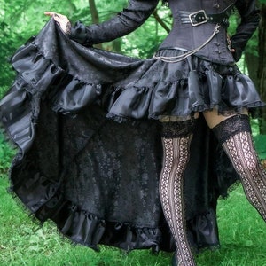 May include: A black, high-low skirt with a ruffled hem and lace trim. The skirt is made of a brocade fabric with a floral pattern. The skirt is paired with black stockings and black shoes.
