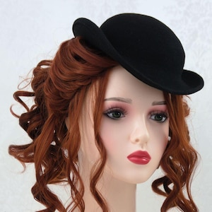 May include: A black felt bowler hat with a wide brim. The hat is small and sits on top of the head.