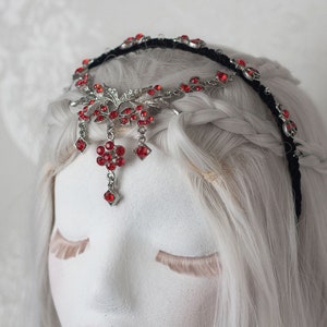 Peut inclure: Un serre-tête argenté avec des embellissements en cristal rouge et un pendentif suspendu. Le serre-tête est orné de feuilles et de fleurs.